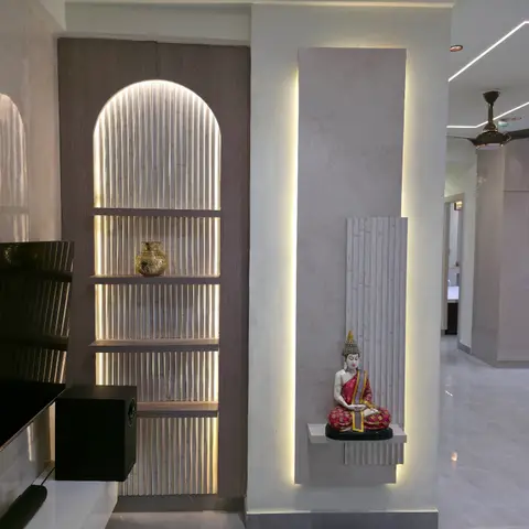 Living room feature wall with a backlit fluted-stone display niche holding a Buddha statue, beside an arched fluted wood shelf niche with a brass vase