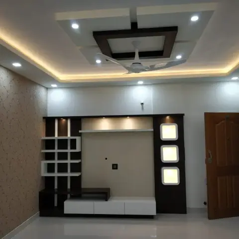 Living room feature wall with a stepped pop false ceiling and cove lighting over a dark-wood TV unit with backlit display niches and floral wallpaper alongside