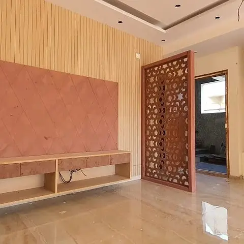 Living room feature wall with a diamond-textured terracotta panel behind a floating TV console, and an ornate jaali screen partitioning the entrance beyond.