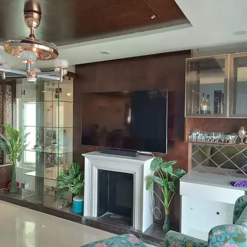 Living room feature wall with a wall-mounted TV over a decorative white mantel, flanked by a mirrored bar cabinet and a tall glass display case