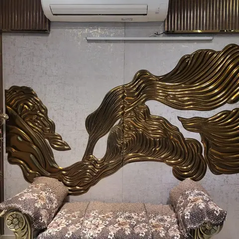 Living room feature wall with a sculptural brass-finish 3D wave art panel above a carved-frame floral-upholstered sofa.