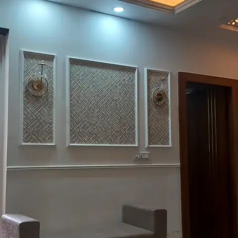 Living room feature wall with three framed textured stone-look panels flanked by wall sconces, under a warm cove-lit ceiling.