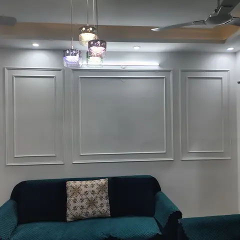 Living room feature wall with three raised panel-moulding frames, a cluster of colored glass pendant lights, and a slipcovered teal-and-navy sofa below.