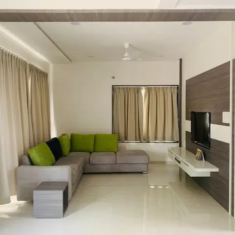 Living room framed by a wood-panelled archway, with a grey L-shaped sofa in olive cushions facing a wall-mounted TV on a laminate feature wall.