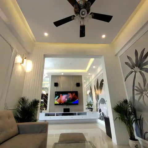 Living room framed by fluted pilaster columns and a cove-lit ceiling, leading to a TV wall with gold string accents and mirror strips