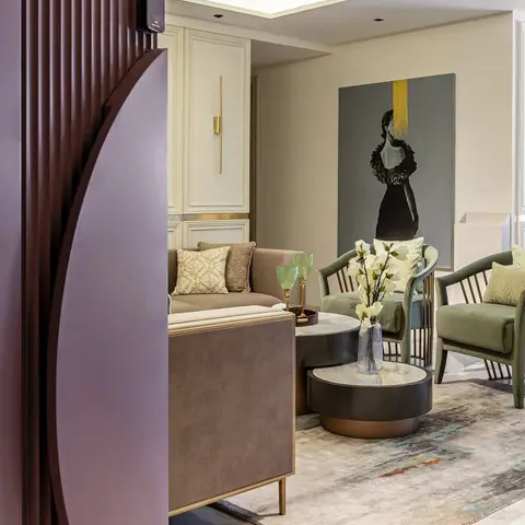 Living room glimpsed through a curved fluted mauve door panel, with olive-green armchairs, a taupe sofa, layered round coffee tables