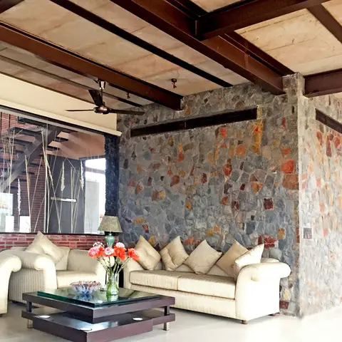 Living room in a villa with a mosaic stone-clad column beneath exposed timber beam ceilings, cream sofas around a glass coffee table.