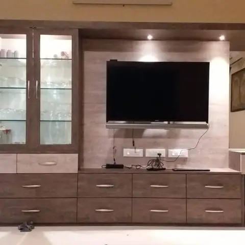 Living room joinery wall combining a glass-front crockery display cabinet with a backlit stone-clad TV panel.