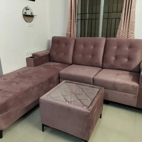 Living room L-shaped sectional sofa in dusty mauve tufted velvet with built-in armrest cup holders, beside a glass-top tufted ottoman.