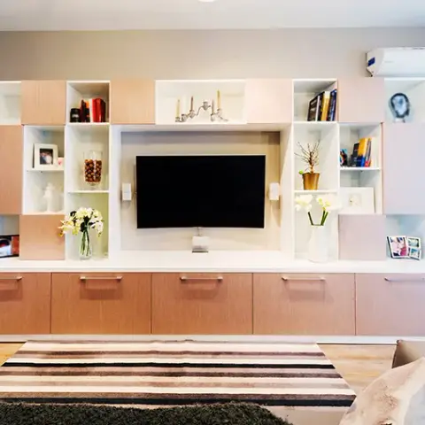 Living-room media wall built from light oak and white modular boxes stepped around a wall-mounted TV, drawers running the full width below