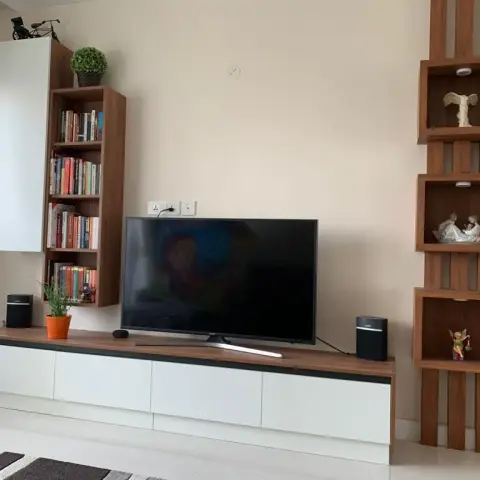 Living-room media wall combining a white and walnut floating drawer console, a slim book tower on the left and three spot-lit walnut display boxes mounted on