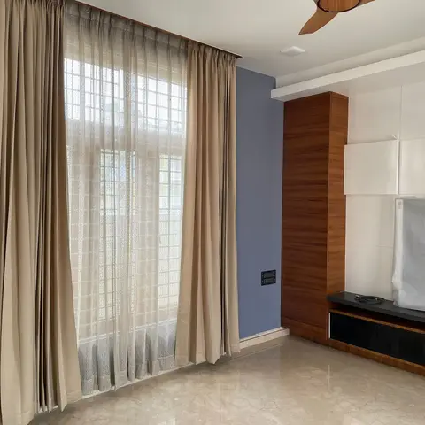 Living room mid-fit-out with a wood-and-white geometric panelled TV wall, a still-wrapped television, floor-length beige curtains with sheer layer
