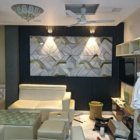 Living room mid-installation: a white-and-gold 3D geometric panel framed in black fluted panelling and grazed by two crystal wall spots