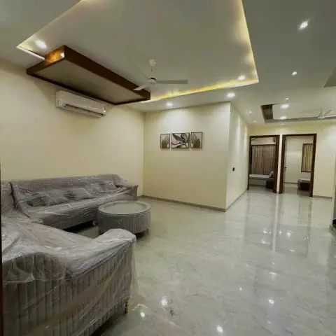 Living room of a just-handed-over flat with the grey L-sofa still in its factory plastic wrap, a fluted round coffee table