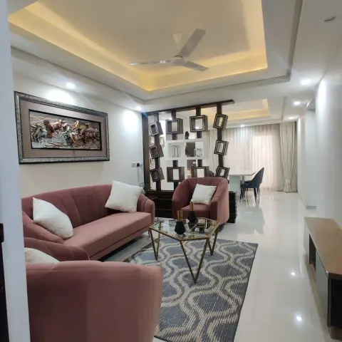 Living room of an Indian flat with a dusty-rose channel-tufted sofa set around a gold hexagonal glass table on an indigo wave-pattern rug