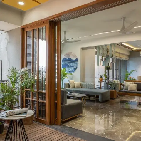 Living room opening through teak-framed glazed folding doors onto a plant-packed balcony deck, with a wooden jhula swing