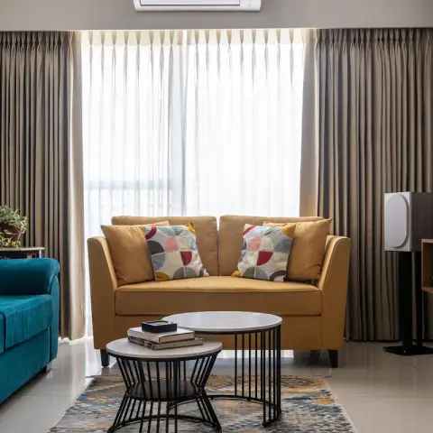 Living room pairing a teal velvet sofa with a mustard-yellow loveseat and colour-block cushions, round black-metal nesting coffee tables