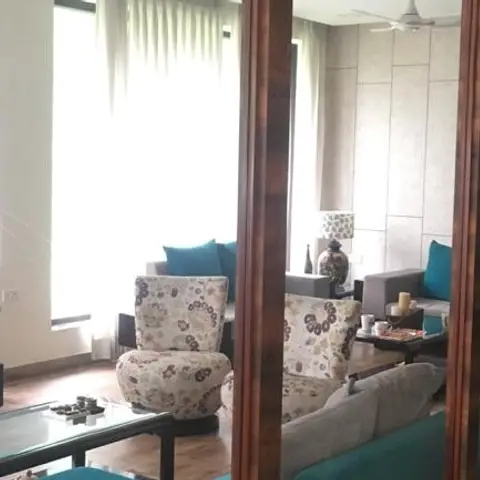 Living room screened by a floor-to-ceiling fluted wood partition, with floral-pattern armchairs and teal cushions around a glass coffee table.