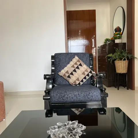 Living room seating area with a black lacquered turned-wood armchair and glass-top coffee table, opening to an entrance foyer with a mirrored console.