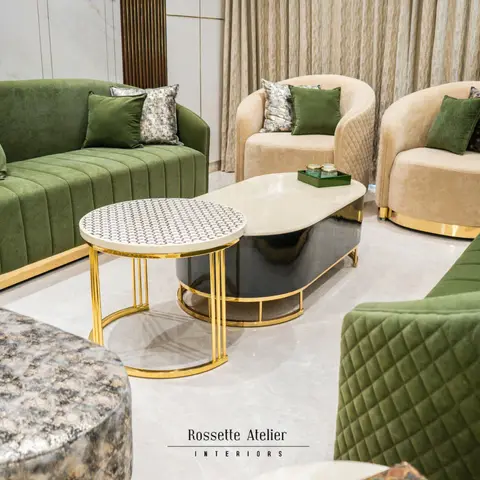 Living room seating arrangement with quilted olive-green velvet sofas, cream tub chairs, and a gold-framed two-tier coffee table with marble accents