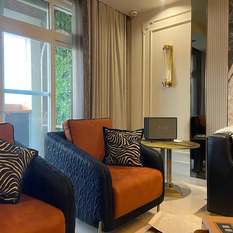 Living room seating nook with rust-and-navy velvet armchairs, zebra-print cushions, a brass wall sconce