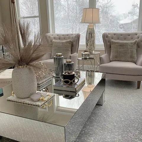 Living room seating nook with two tufted wingback armchairs and a mirrored coffee table styled with a curated vignette of vases and books.