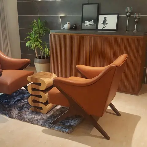 Living room seating nook with two tan leather mid-century armchairs around a sculptural wood stool table