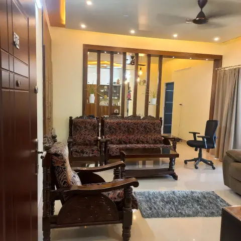 Living room seen from the open front door: a carved teak sofa set in printed upholstery on gloss ivory tiles