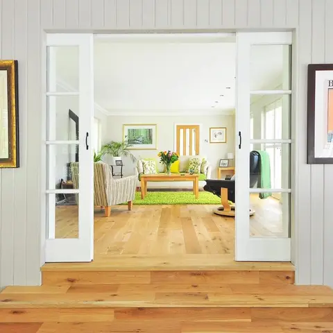 Living room seen through open glass French doors, with a striped armchair, a sofa dressed in yellow and green cushions