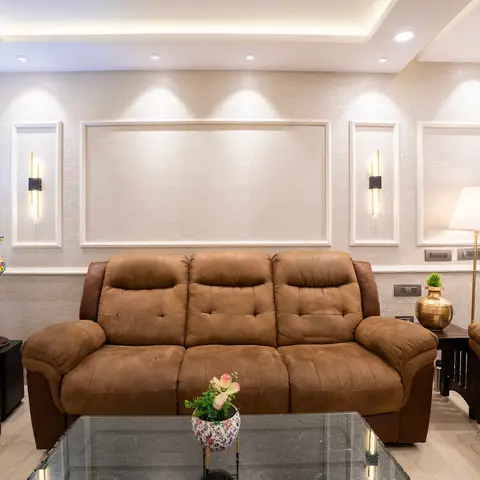 Living room sofa in tan suede-look upholstery against a cream wall with framed moulding panels and brass wall sconces