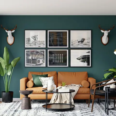 Living room styled in mid-century modern furniture, with a tan leather sofa and walnut-frame armchair against a deep teal accent wall hung with a