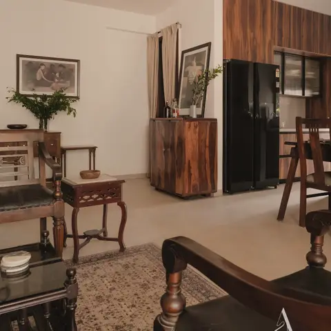 Living room styled with dark wood colonial-era furniture — a carved campaign chair, an inlaid side table and console tables — framed art on cream walls