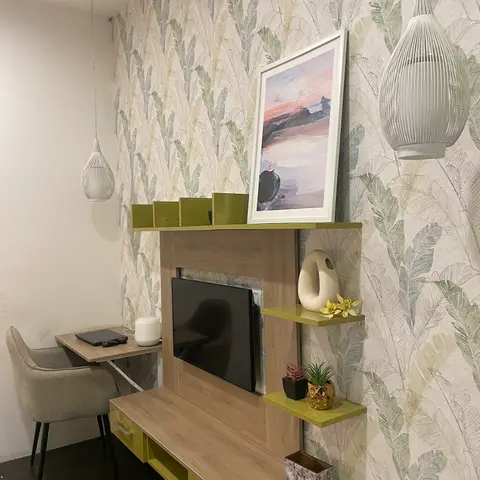 Living room TV console in wood and olive-lacquer finish against a botanical leaf-print wallpaper wall, with cage pendant lights and a framed sunset print.