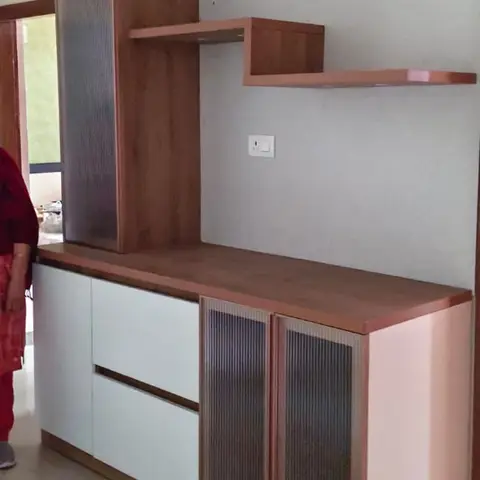 Living room TV console unit with fluted glass cabinet doors, white drawer fronts, and a floating wood corner shelf on a plain grey accent wall.