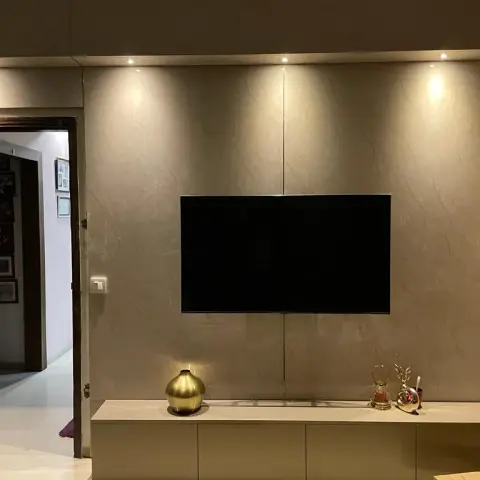Living room TV feature wall clad in book-matched beige stone-look panels with recessed spotlights
