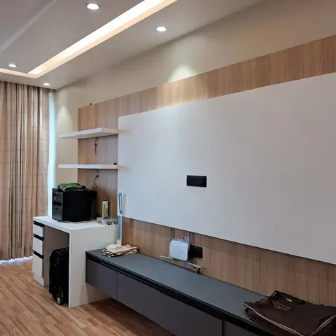 Living room TV feature wall combining white lacquer and wood-laminate panelling above a floating dark grey console, with a cove-lit stepped false ceiling.
