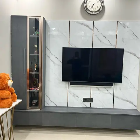Living room TV feature wall in white marble-effect panelling with rose-gold trim strips, floating grey console, and a glass display cabinet with trophies.