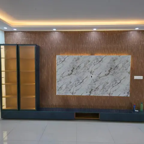 Living room TV feature wall in fluted bronze-toned panelling with a backlit marble slab centerpiece and a tall glass-front display cabinet.