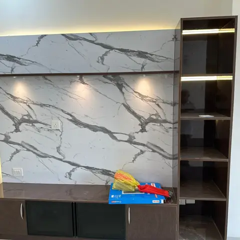 Living room TV feature wall in a large-format grey-veined marble slab, paired with a dark wood-veneer TV console and a backlit open display shelving unit.
