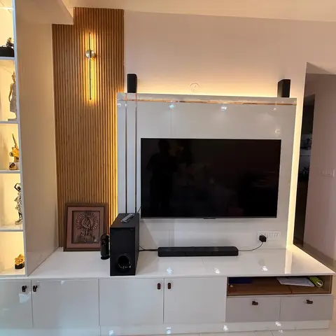 Living room TV feature wall in glossy white with a backlit fluted-wood accent panel, flanked by a lit display shelf styled with brass figurines.