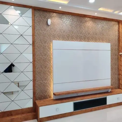 Living room TV feature wall with damask gold wallpaper, a geometric diamond-cut mirror panel on one side and chevron-pattern wood shelving on the other.