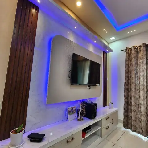 Living room TV feature wall with a marble-effect panel, wooden fluted side borders and blue cove lighting under a false ceiling.