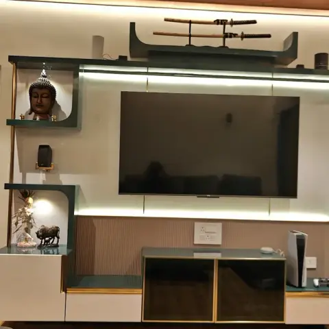 Living room TV feature wall with white-and-emerald-green panelling, gold trim accents, backlit LED niches displaying a Buddha head and idol curios