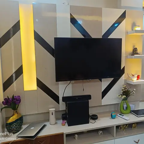 Living room TV feature wall with a beige and black geometric chevron panel design, a backlit vertical accent strip, floating curio display shelves