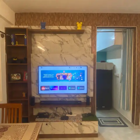 Living room TV feature wall with a marble panel in a wood frame, open display shelving with personal items, and a soundbar below a wall-mounted television.