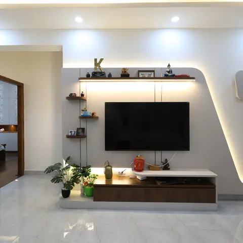 Living room TV feature wall with a diagonal cove-lit cutout, floating corner display shelves styled with brass idols and framed photos