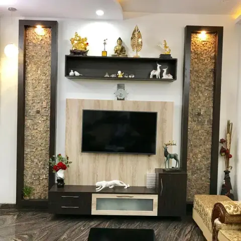 Living room TV unit flanked by mosaic stone-tile pilasters, topped with an open display shelf styled with a brass Buddha statue and curios