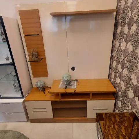Living room TV unit in cream gloss and wood-laminate finish beside a glass-front bar cabinet, set against a brown diamond-patterned accent wallpaper.