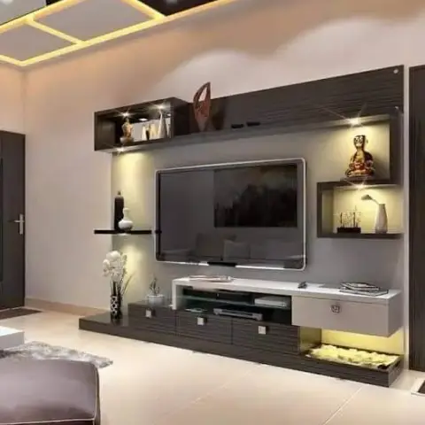Living room TV unit in dark wood-grain panelling with open display shelves holding a Buddha statue and vases, below a backlit geometric-grid false ceiling.