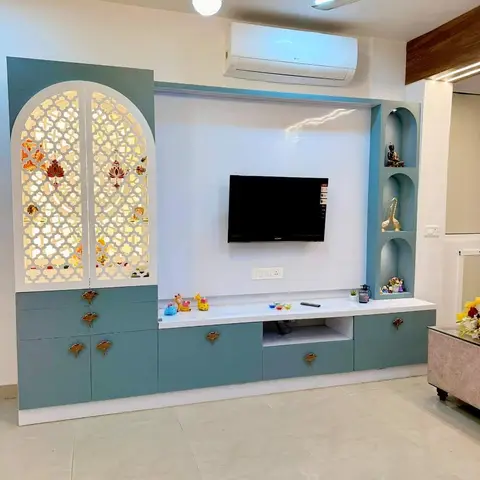 Living room TV unit in teal with an integrated backlit arched jaali-door pooja cabinet and a gold ring pendant light overhead.